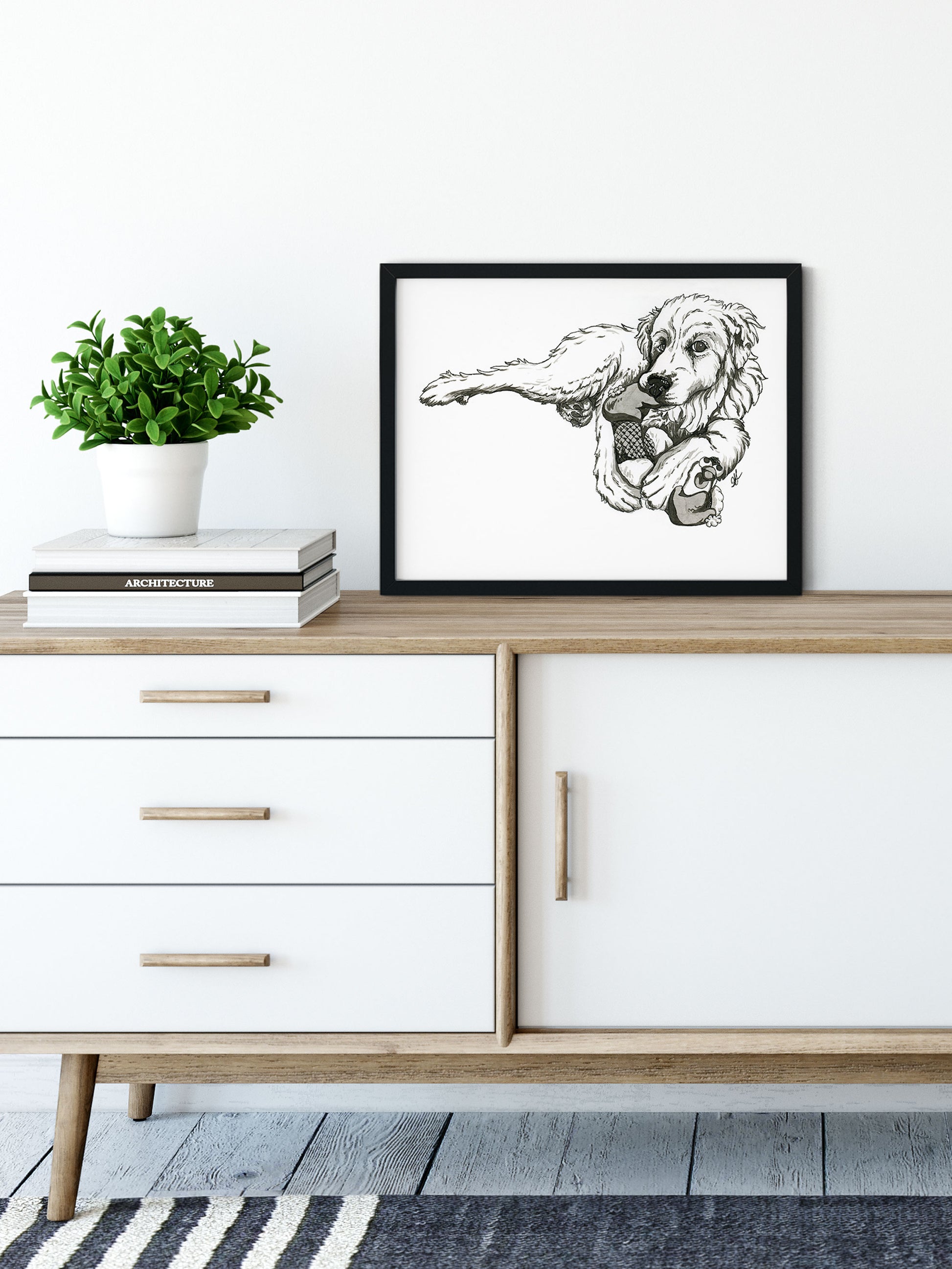 A frames giclee fine art print of pen and ink illustration of a great pyrenees dog chewing on a chicken stuffie toy placed in a modern home. By Heidi Leduc